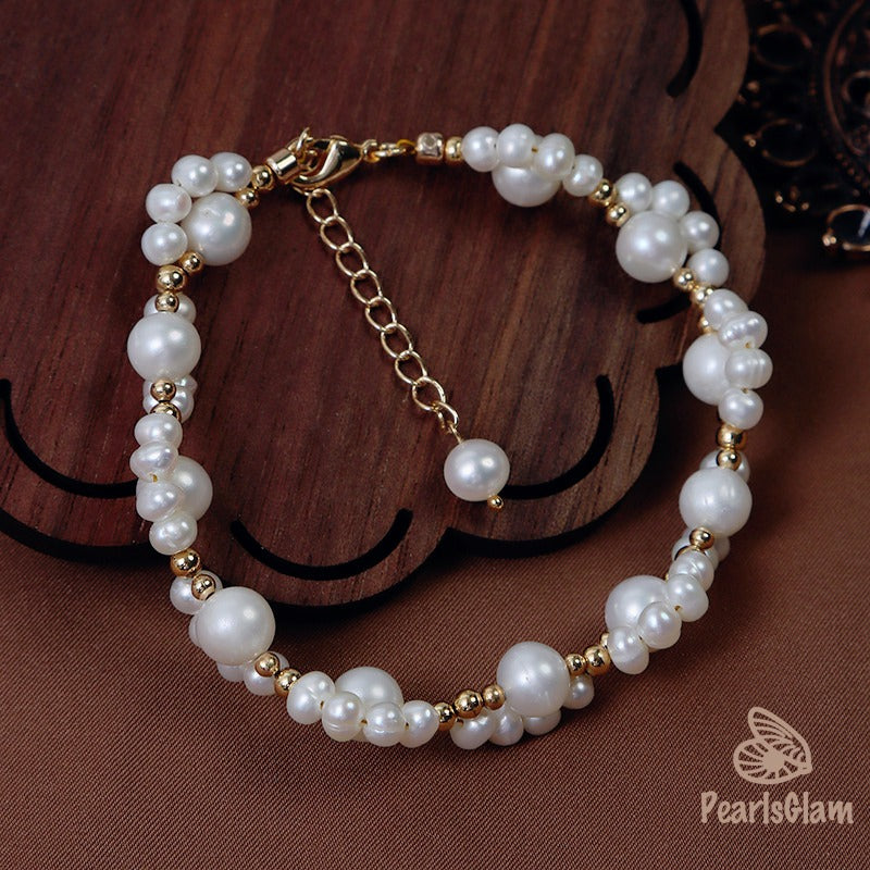 Pearl bracelet with gold accents on a wooden surface, branded 'PearlsGlam'.