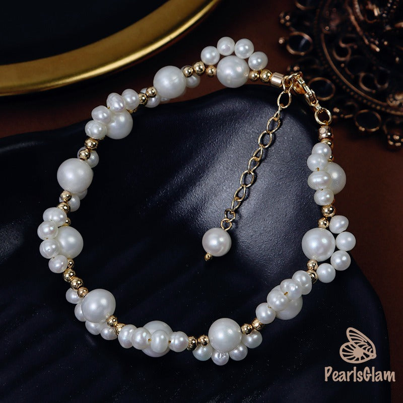 Pearl bracelet with gold accents on a dark fabric background, branded 'PearlsGlam'.